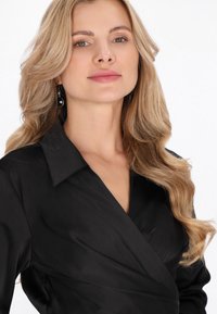 Černá zavinovací halenka s límečkem, dlouhými rukávy a měkkou, hladkou texturou s jemným řasením vpředu.