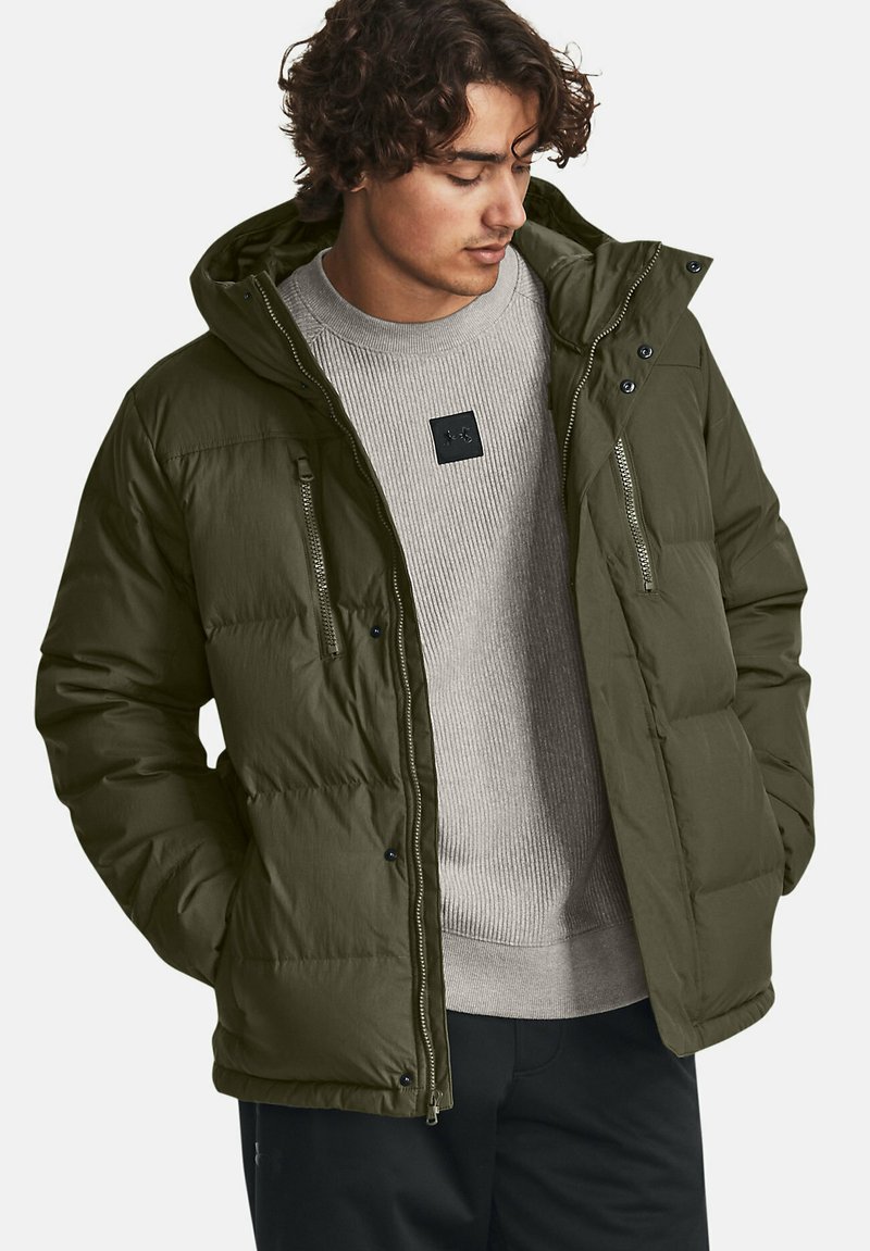 Opgeblazen olijfgroene jas met een capuchon, met ritszakken en een geribbelde grijze trui eronder. Gestoffeerd materiaal met een gladde afwerking.