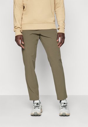Sweatshirt beige clair associé à un pantalon vert olive. Le pantalon est fuselé et lisse avec des poches latérales. La chaussure est blanche avec des lacets noirs.
