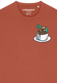 T-shirt en coton couleur rouille avec un motif d'une tasse entourée de montagnes, de palmiers et d'une planche de surf, détaillé en blanc et en vert.