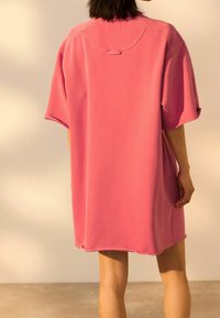 Overmaatse roze katoenen jurk, korte mouwen, ronde hals, ruwe randen, ontspannen pasvorm, zijsplit, gladde textuur, casual stijl.
