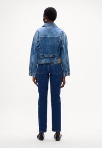 Giacca di jeans blu con un design aderente, lunghezza corta e dettagli con bottoni. Abbinata a jeans scuri a gamba dritta.