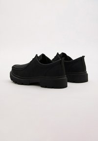 Zapatos de cuero negro con puntera redondeada, superficie texturizada y suela de goma gruesa con profundas ranuras para tracción. Dos tiradores en el talón.