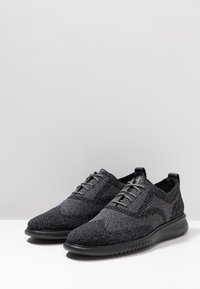 Sneaker nere in maglia con una parte superiore testurizzata, design con lacci e suola nera flessibile. Stile minimalista senza logo visibile.