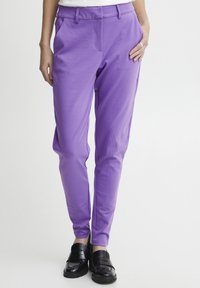 Lila byxor med en slät tygfinish, med en avslappnad passform, framfickor och en midjehög linning. Kända med svarta loafers.