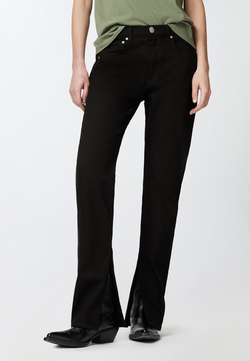 Jeans negros acampanados de mezclilla, con aberturas laterales en el dobladillo y herrajes plateados. Combinados con botas negras de tobillo.