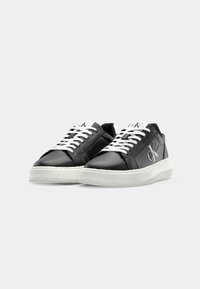 Fekete bőrsneaker fehér fűzőkkel és texturált gumitalppal. Az oldalon logó található, valamint párnázott gallér a kényelemért.
