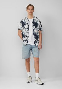 Korte mouwen navy en witte palm-gepatroneerde shirt, wit T-shirt met ronde hals, lichte denim shorts, witte sokken en neutraal gekleurde sportschoenen.