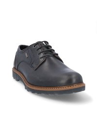 Zapato de cuero negro con punta redondeada, diseño de cordones, suela de goma marrón y costuras en contraste a lo largo del borde. Acabados texturizados en los laterales.