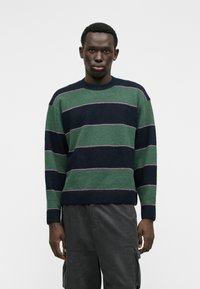 Maglione di lana lavorato a maglia con strisce verdi e blu navy, arricchito da sottili accenti rosa; scollatura rotonda e polsini e orlo a coste.