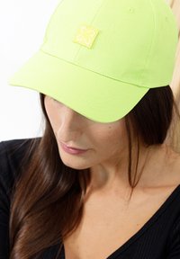 Neon-grüner Baseball-Cap aus Stoff, mit einem gelben gestickten Logo auf der Vorderseite und einem gebogenen Schirm.