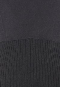 Musta neulemekko, jossa on sileä yläosa ja texturoitu ribbireuna. Kangas on tasalaatuinen, tarjoten yhtenäisen tumman sävyn kauttaaltaan.