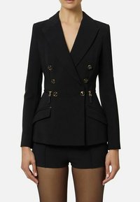 Blazer nero doppiopetto con bottoni dorati, rever appuntito e tasche con cerniera. Vestibilità sartoriale con spalle strutturate e maniche lunghe.