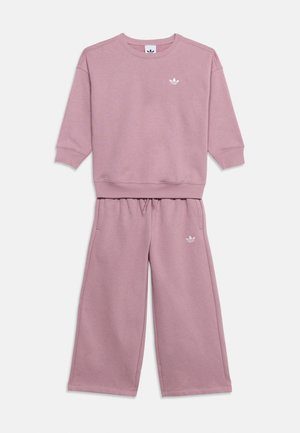 Liliowy zestaw z bluzy z długim rękawem i spodniami o szerokich nogawkach z logo Adidas na klatce piersiowej i udzie, wykonany z miękkiego materiału.