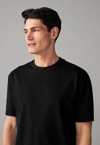 Black cotton T-shirt with short sleeves and a round neckline. Smooth texture, relaxed fit, and minimalistic design without visible logos.