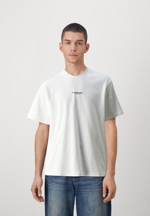 T-shirt bianca in cotone con maniche corte e scollo rotondo. Presenta un piccolo logo nero sul petto e una vestibilità comoda. Abbinata a jeans in denim.