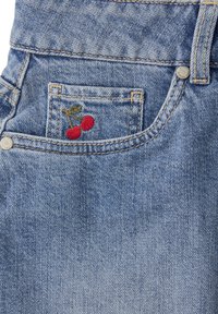 Poche de jean en denim avec de petites cerises rouges brodées et des feuilles vertes sur la poche à monnaie, coutures visibles et rivets argentés.