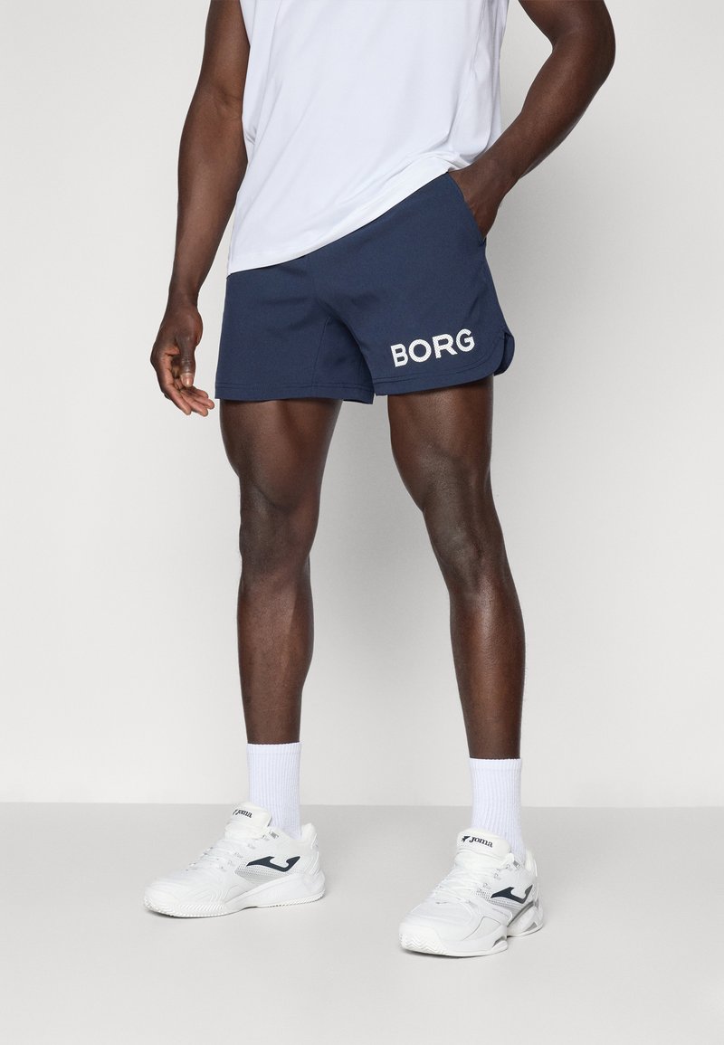 Calções masculinos em azul-marinho feitos de tecido leve, apresentando letras brancas "BORG" na perna esquerda. Estilo descontraído e com bolsos.