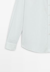 Lichtblauw langekatoenen shirt met een gladde afwerking. Heeft een puntige kraag, knoopsluiting aan de voorkant en een afgeronde zoom. Met manchet mouwen.