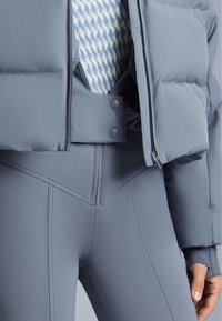 Pamučena siva jakna s visokim ovratnikom, zatvaranjem na zip i detaljima na gumbima, uparena sa uskim sivim tajicama s dizajnom šava.