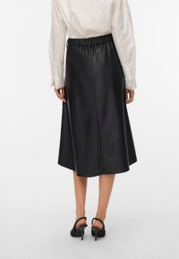 Jupe midi en cuir noir avec une taille élastique, présentant une texture lisse et un design évasé, associée à des chaussures à talons hauts noires.