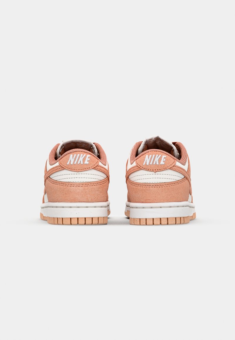 Sneakers Nike Dunk Low en suède rose doux avec des accents en cuir blanc et une semelle intermédiaire blanche texturée. Logo positionné sur le talon, semelle extérieure en caoutchouc translucide.