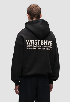 Black cropped hoodie with large white lettering on the back. Features a hood, long sleeves, and ribbed cuffs for added texture.