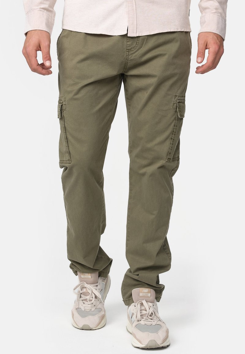 Pantalones cargo en una mezcla de algodón verde olivo, con bolsillos laterales, un ajuste relajado y detalles de costura sutiles, combinados con zapatillas de color claro.