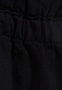 Svart tyg med en texturerad väv, med samlad sömnad längs kanten som skapar en serie mjuka veck.