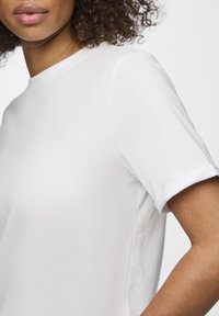 Weißes T-Shirt mit Rundhalsausschnitt und kurzen umgeschlagenen Ärmeln, aus glattem, leichtem Stoff, das eine figurbetonte Silhouette und minimalistische Nähte zeigt.