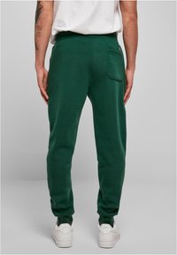 Groene joggingbroek van zacht materiaal, met een achterzak, taps toelopende pijpen en een elastische tailleband, gecombineerd met witte sneakers.
