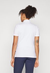 White polo shirt with a collar, short sleeves, and a smooth texture. Features a side slit near the hem for ease of movement.