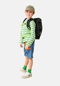 Zwarte rugzak met groene geometrische accenten, groen en wit gestreepte langemouwen shirt, blauwe denim shorts, witte schoenen met groen logo.