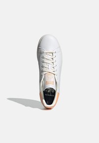 White leather sneaker with a smooth texture, light beige laces, and a peach accent on the heel. Features a printed logo on the tongue.