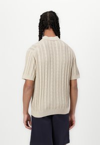 Beige kötött pulóver rövid ujjakkal, függőleges bordás mintázattal és kerek nyakkal. Puha textúra, nyitott szövéssel.