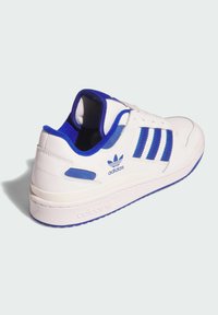 White sneaker with blue accents, featuring three stripes, padded collar, and textured rubber sole. Branding on heel and side.