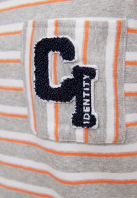 Tessuto a strisce grigio e bianco con accenti arancioni. Presenta una toppa texturizzata con "C1" e "IDENTITY" ricamati in blu.