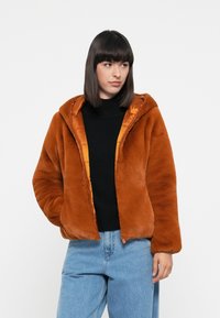 Roodoranje pluche jack met capuchon, voorzien van een glanzende oranje voering, frontzipper en lange mouwen; gecombineerd met blauwe jeans.