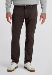 Pantalons chinos en coton marron avec une coupe ajustée, dotés de poches avant, d'une fermeture à bouton et de coutures contrastées. Portés avec des sneakers blanches.