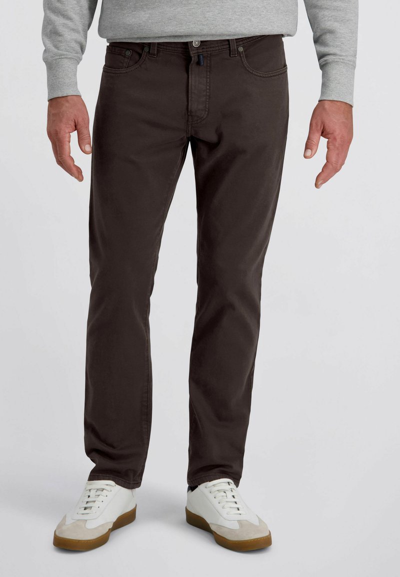 Pantalons chinos en coton marron avec une coupe ajustée, dotés de poches avant, d'une fermeture à bouton et de coutures contrastées. Portés avec des sneakers blanches.