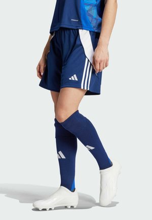 Marinevoetbalkorte broek met witte zijkanten, gecombineerd met knielange blauwe sokken met witte accenten. Witte voetbalschoenen.