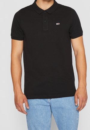 Polo noir en coton, avec un col, des manches courtes et un petit logo sur la poitrine. Associé à un jean bleu clair.