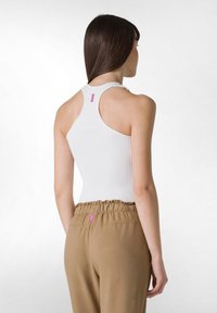 Top sin mangas blanco con diseño de espalda nadadora, combinado con pantalones de cintura elástica beige que presentan una pequeña etiqueta rosa en la parte posterior.