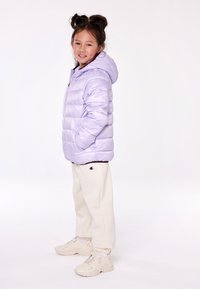 Giacca a vento viola chiaro con cappuccio, design trapuntato. Abbinata a pantaloni felpati crema e sneaker beige con un discreto branding.
