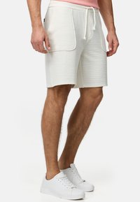 Pantalones cortos texturizados blancos con cintura ajustable, que cuentan con dos bolsillos laterales y un corte relajado. Combinados con zapatillas blancas.