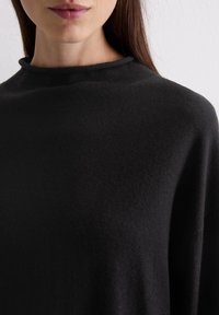 Schwarzer, strukturierter Strickpullover mit hohem Kragen und lockerer Passform, der eine glatte Oberfläche und minimale Nähte zeigt.