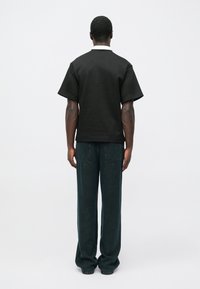 Fekete, rövid ujjú póló kerek nyakkal, széles sötét farmer nadrággal, melyen két hátsó zseb található. Minimalista kialakítás, egyszínű.