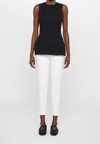 Svart ärmlös topp med rak skärning, med knäppning framtill. Matchas med vita slim-fit byxor och svarta platta skor med nitar.