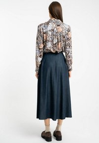 Długo-sleeve bluzka w kwiatowy wzór w odcieniach brązu, niebieskiego i brzoskwiniowego; zestawiona z ciemnoniebieską spódnicą dżinsową, która sięga kostek.