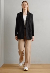 Černý pruhovaný blazer přes bílé tričko, doplněný béžovými kalhotami širokého střihu a bílými teniskami. Hladký, šitý na míru s klasickou siluetou.